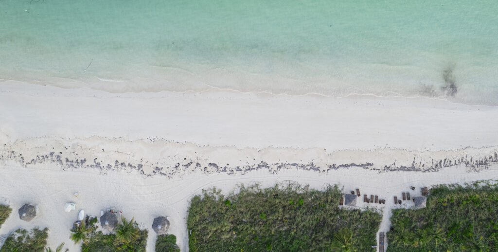 aerial view of a Freeport, Grand Bahama beach: clear turquoise water, gentle surf, white sand, and dark limestone rocks along the shore.